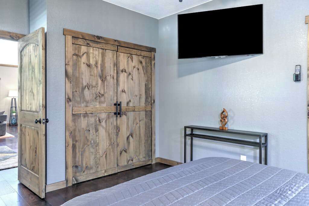 A bedroom with a bed, a wooden wardrobe, a mounted TV, and a small table with a decorative item.