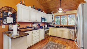 Una cucina con mobili bianchi, un forno a microonde, un frigorifero e un soffitto in legno.