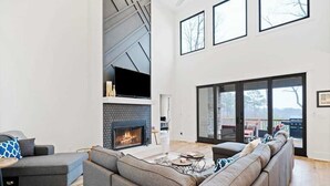 A modern living room with a fireplace, a sectional sofa, and a large window. - Knight Mountain Stay (Ellijay)