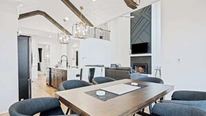 A modern kitchen with a central island, a dining area with a wooden table and chairs, and a fireplace. - Knight Mountain Stay (Ellijay)