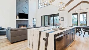 A modern kitchen with a large island, a built-in fireplace, and a dining area with a view. - Knight Mountain Stay (Ellijay)