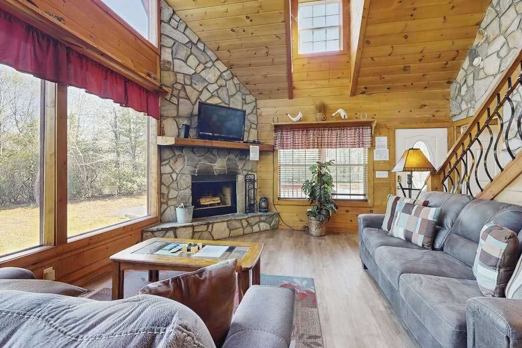 Ein gemütliches Blockhaus-Interieur mit Kamin aus Stein, Holzwänden, einer Couch und einem Fernseher.