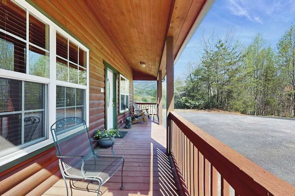 A wooden cabin with a porch, a bench, and a view of the surrounding forest.