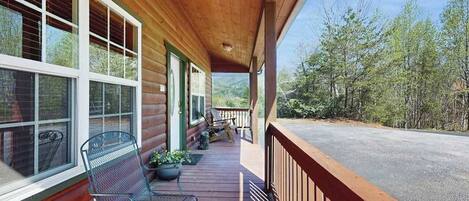 A wooden cabin with a porch, a bench, and a view of the surrounding forest.