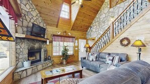 Ein gemütliches Blockhauss-Interieur mit Kamin, Sofa, Fernseher und Treppe.