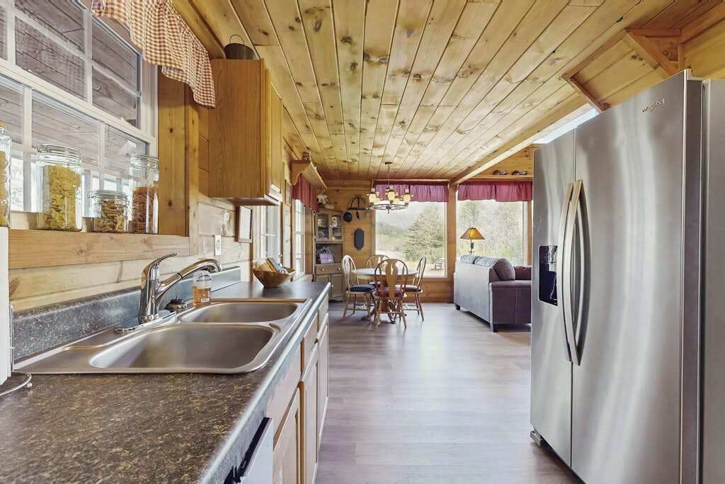 A wooden cabin interior with a kitchen, dining area, and a large refrigerator.