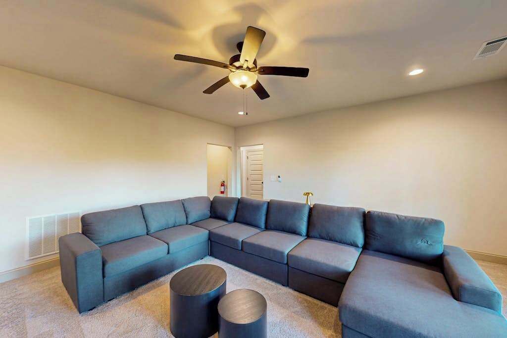 A modern living room with a sectional sofa, a ceiling fan, and a small round table.