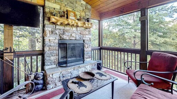 A stone fireplace with a TV, a red chair, and a table with placemats. - Cherokee Sunrise Cabin (Mineral Bluff)