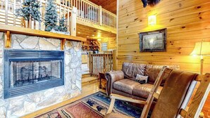 A log cabin interior with a stone fireplace, leather sofa, and a wooden deck. - Cherokee Sunrise Cabin (Mineral Bluff)