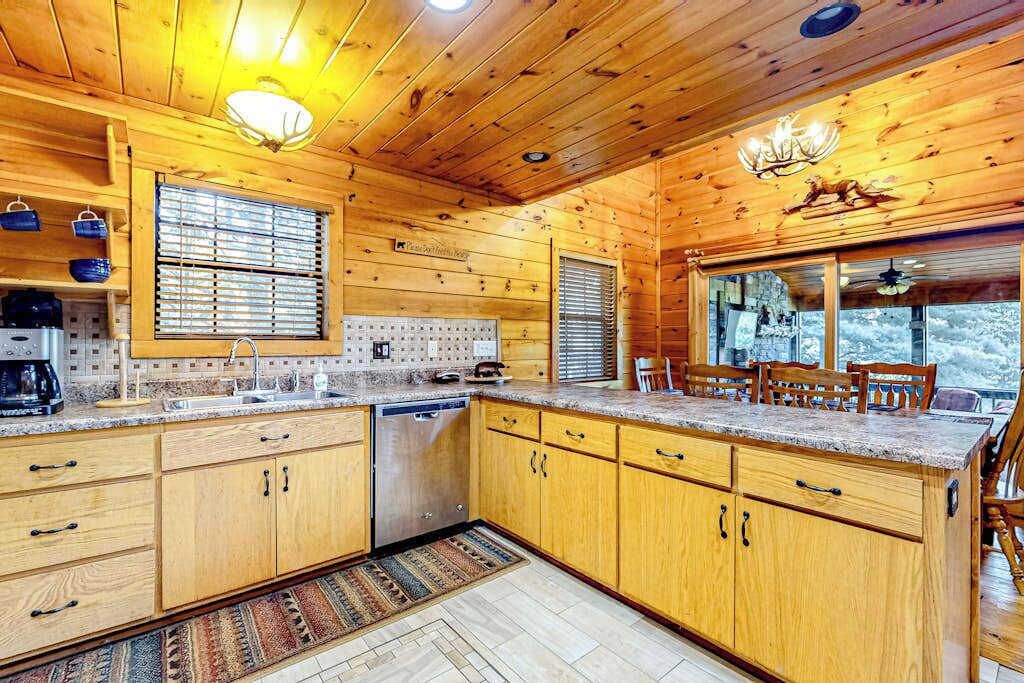 A wooden cabin interior with a kitchen, dining area, and a large window.