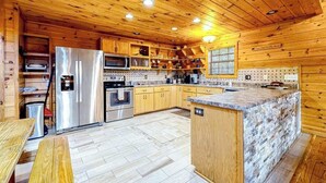 A wooden cabin-style kitchen with a central island, built-in appliances, and a dining area. - Cherokee Sunrise Cabin (Mineral Bluff)