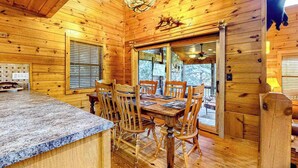 A wooden cabin interior with a dining table, chairs, a chandelier, and a large window. - Cherokee Sunrise Cabin (Mineral Bluff)