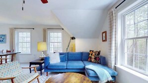 Een woonkamer met een blauwe bank, een ronde houten salontafel, een lamp en een raam met gordijnen.