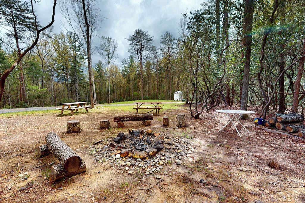 A campsite with a fire pit, picnic tables, and a tent.
