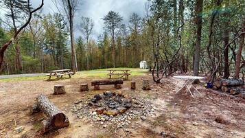 A campsite with a fire pit, picnic tables, and a tent.