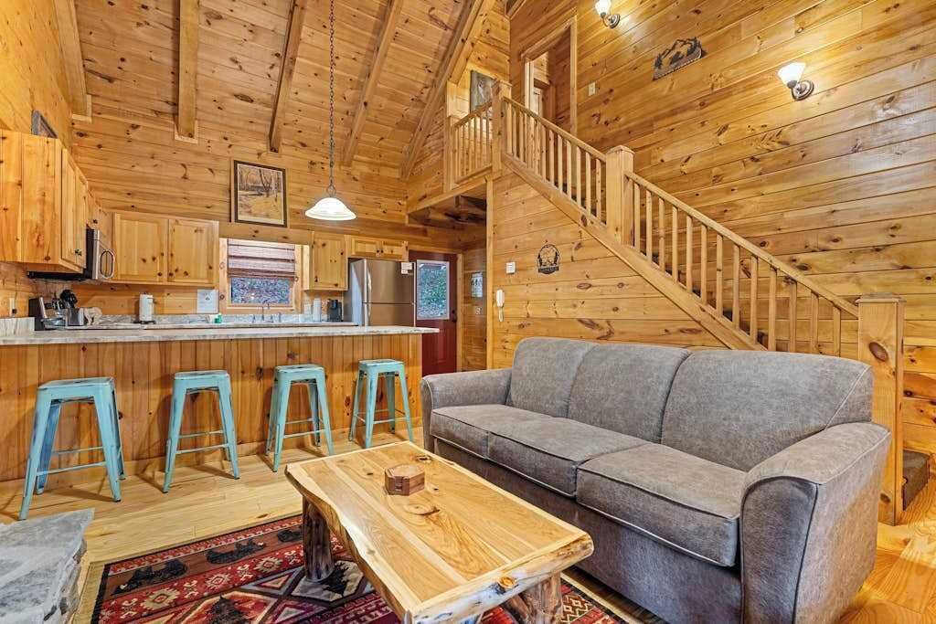 L’intérieur d’un chalet en bois comprend une cuisine, des tabourets de bar, un canapé et un escalier.