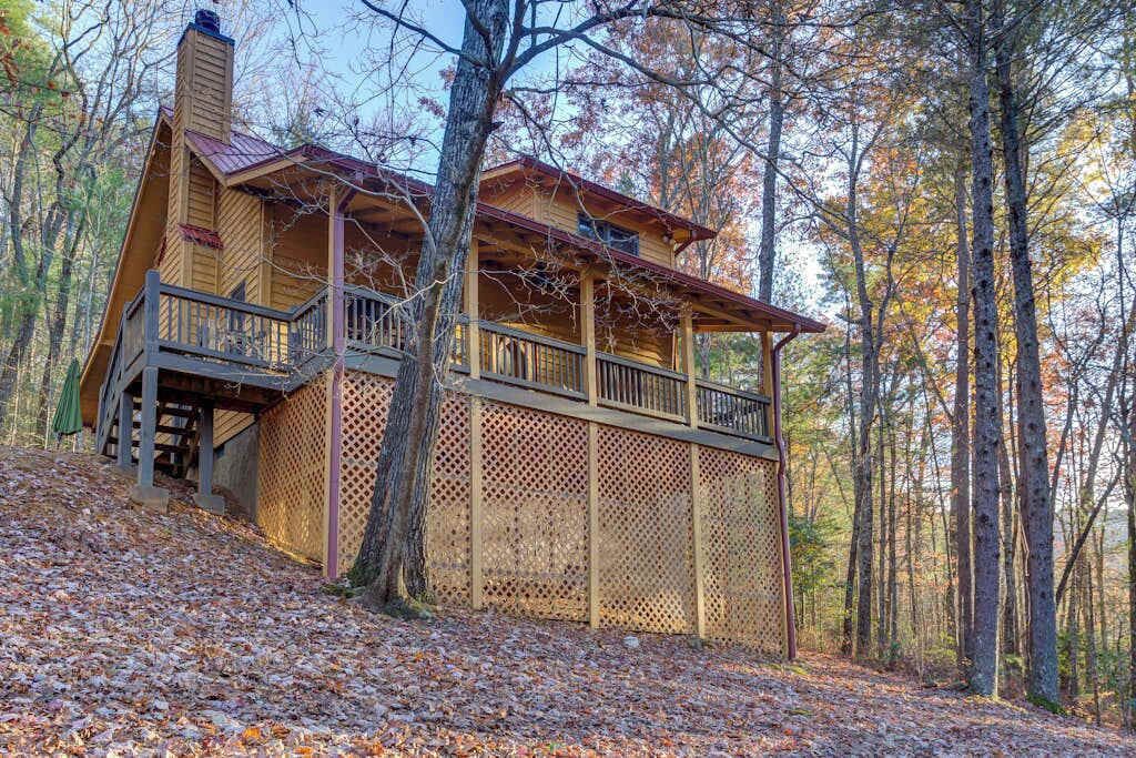 Une cabane en bois dotée d’un balcon, entourée d’arbres et recouverte de feuilles mortes.