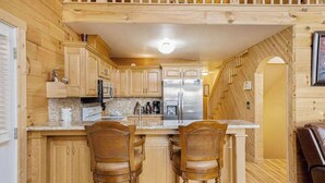 A wooden cabin interior with a kitchen featuring wooden cabinets, a stainless steel refrigerator, and a dining area with two wicker chairs. - House of Views Getaway (Blue Ridge)