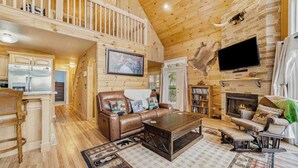 A log cabin interior with a living room, kitchen, and dining area, featuring wooden floors, a fireplace, and a mounted television. - House of Views Getaway (Blue Ridge)