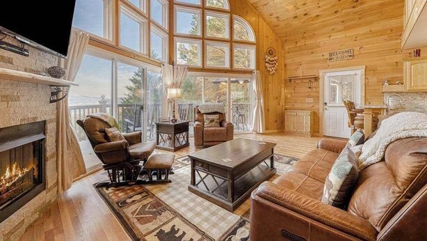 A spacious living room with a fireplace, leather furniture, large windows, and a wooden ceiling. - House of Views Getaway (Blue Ridge)