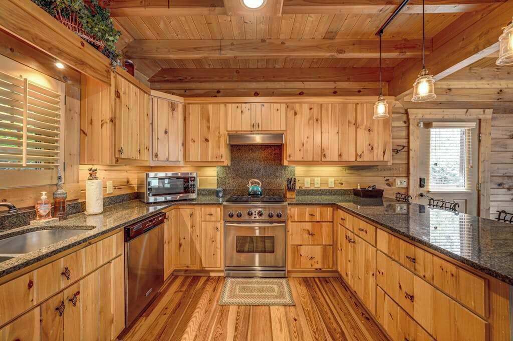 Interior de una cabaña de madera con cocina, que incluye encimeras de granito, armarios de madera, estufa y microondas.