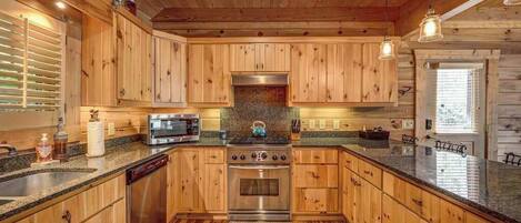 Interior de una cabaña de madera con cocina, que incluye encimeras de granito, armarios de madera, estufa y microondas.