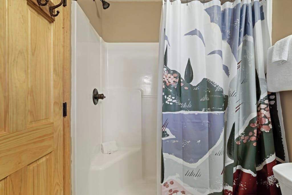 A bathroom with a shower curtain, a wooden door, and a white bathtub.