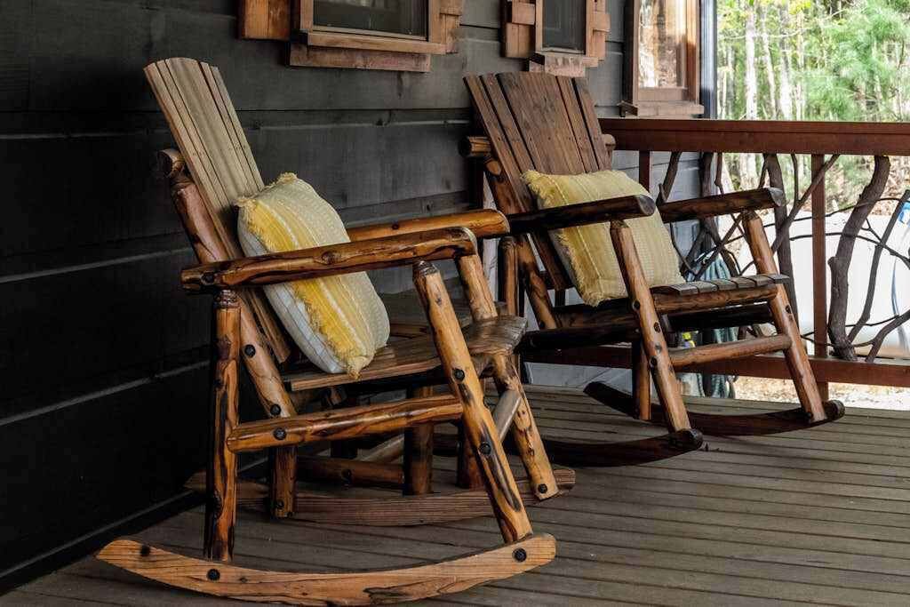 Dos mecedoras de madera con cojines sobre una terraza de madera.