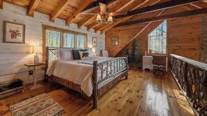 Quarto de cabana de madeira com cama, escrivaninha, cadeira, uma pequena árvore de Natal e janela.