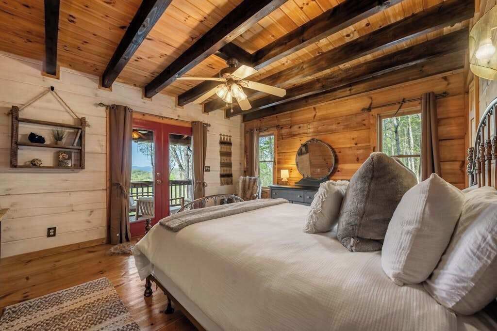 Ein Schlafzimmer einer Holzhütte mit einem Bett, einem Deckenventilator und Blick ins Freie.