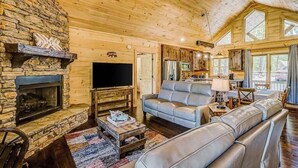 Ein gemütliches Blockhaus-Interieur mit Kamin aus Stein, Ledersofa und Fernseher.