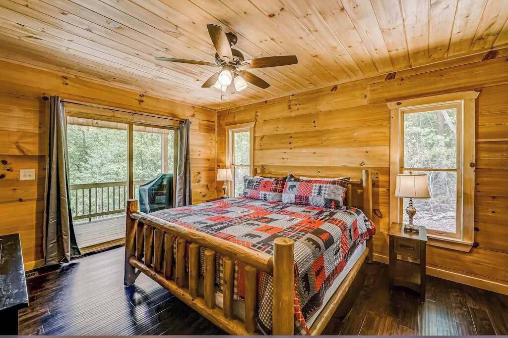 Un dormitorio de cabaña de madera con una cama, un ventilador de techo y una ventana.