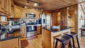 Interior de uma cabana de madeira, com cozinha equipada com fogão, micro-ondas, frigorífico e banquetas.