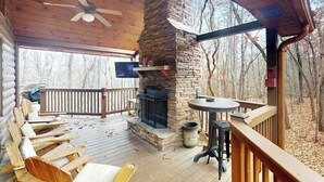 A wooden deck with a stone fireplace, a TV mounted on the wall, and outdoor seating. - Blue Ridge Bear Bungalow (Blue Ridge)