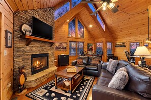 A cozy cabin interior with a stone fireplace, leather furniture, and large windows offering views of the outdoors. - Blue Ridge Bear Bungalow (Blue Ridge)
