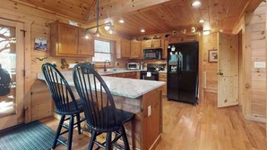 A wooden cabin-style kitchen with a central island, two bar stools, a refrigerator, a microwave, and a sink. - Blue Ridge Bear Bungalow (Blue Ridge)