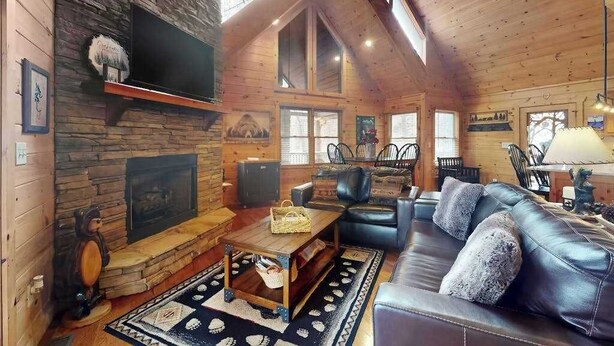 A cozy cabin interior with a stone fireplace, leather sofa, and a television mounted on the wall. - Blue Ridge Bear Bungalow (Blue Ridge)