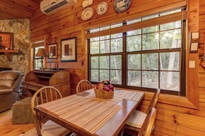 A wooden cabin interior with a dining table, chairs, a stone wall, and a large window. - River Ranch Ellijay Stay (Ellijay)