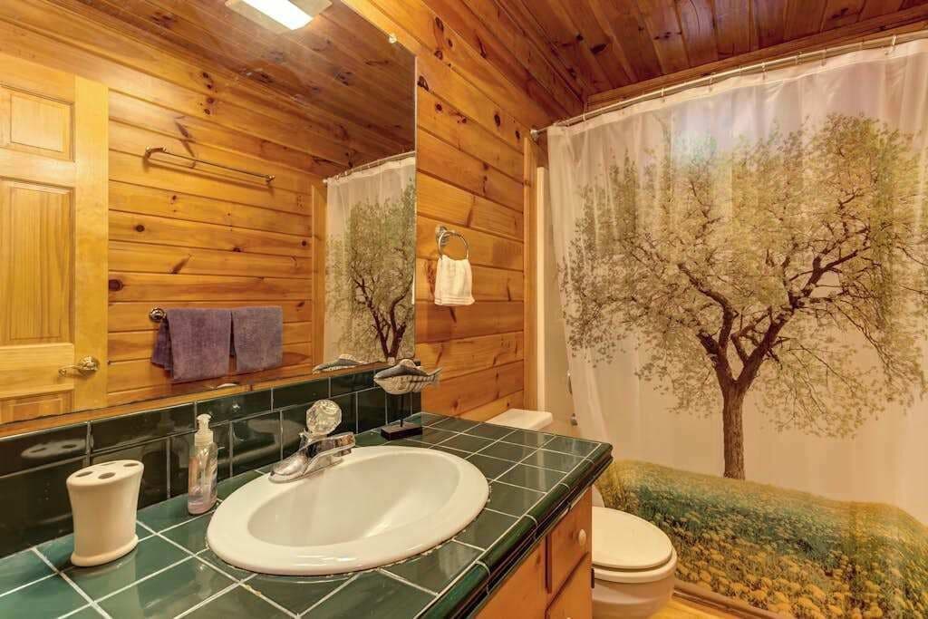 A bathroom with wooden walls, a sink, a toilet, and a shower curtain with a tree design.