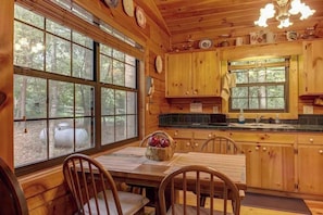 A wooden cabin kitchen with large windows, a dining table, chairs, and a fruit basket. - River Ranch Ellijay Stay (Ellijay)