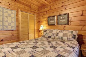 A wooden cabin bedroom with a quilted bedspread, a closed wooden door, and two framed pictures on the wall. - River Ranch Ellijay Stay (Ellijay)