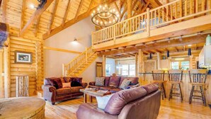 Ein großzügiges Holzhaus-Interieur mit hohen Decken, einer Treppe, einem Wohnzimmer mit Ledersofas und einer Küchenzeile.