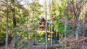 Ein Waldhaus mit einer Holzterrasse und einem Schornstein, umgeben von Bäumen und Grün.
