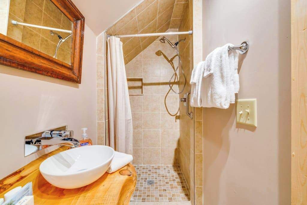 A bathroom with a wooden vanity, a white sink, a mirror, a shower with a glass door, and a towel rack.