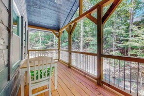 Una terraza de madera con una silla blanca, rodeada de un bosque.
