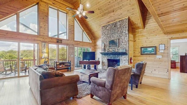 Un salón espacioso con chimenea de piedra, techo de madera y ventanas amplias.