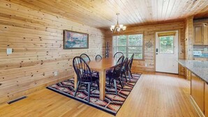 Un interior de madera con una mesa de comedor, sillas, una araña y vistas a través de una ventana.