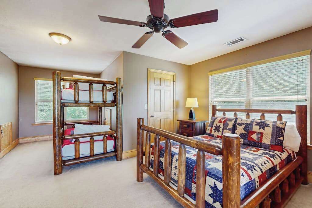 Ein Zimmer mit Etagenbetten, einem Deckenventilator, einem Fenster mit Jalousien und einem Nachttisch mit Lampe.