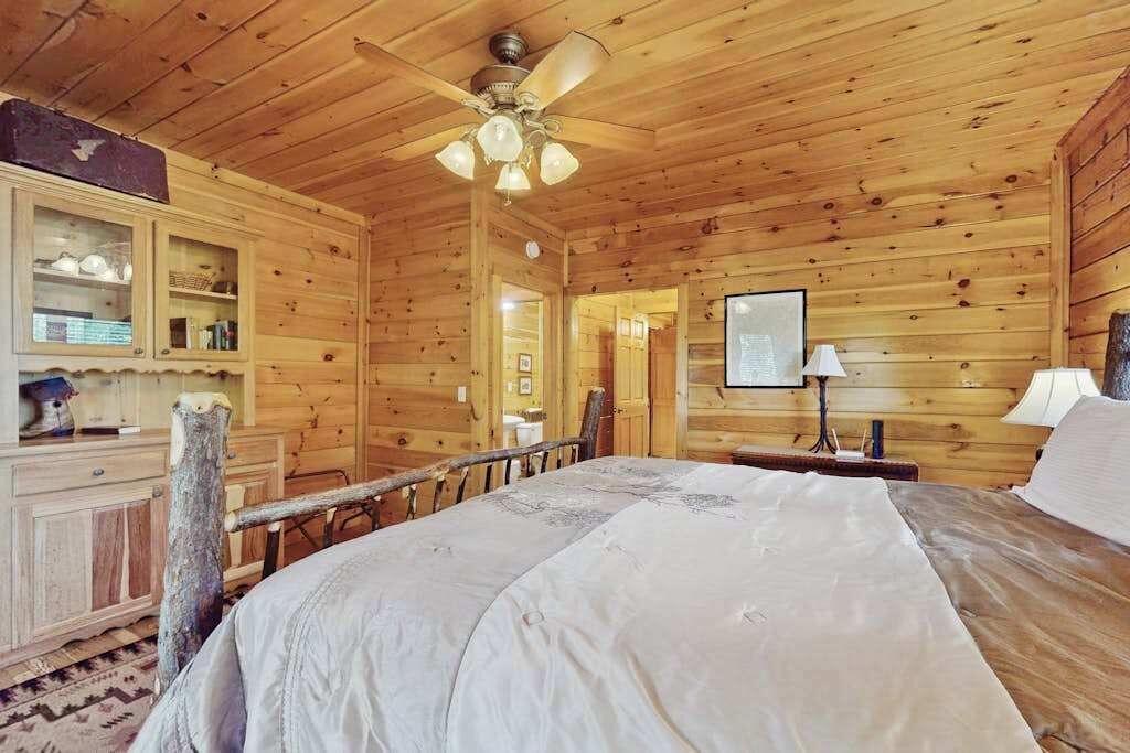 A wooden cabin room with a bed, a ceiling fan, a wooden dresser, and a framed picture on the wall.
