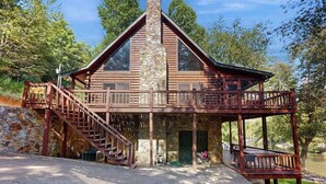 A log cabin with a stone chimney, wooden balcony, and a staircase leading to an upper level. - River Escape On The Toccoa River (Mineral Bluff)